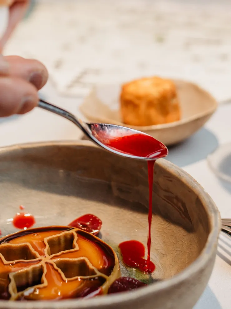 Gourmet dish with berry sauce being plated alongside glass of white wine