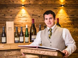 Weinexperte präsentiert Müller Weine vor rustikaler Holzwand mit Flaschen und Geschenkbox
