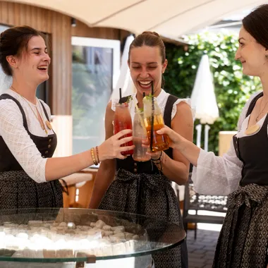 Women in traditional dirndl dresses toasting with colorful summer drinks outdoors