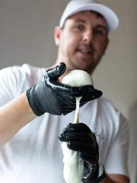 Mann formt frischen Mozzarella mit schwarzen Handschuhen