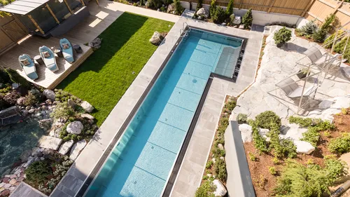 Modern backyard with rectangular swimming pool, lounge area, and landscaped garden