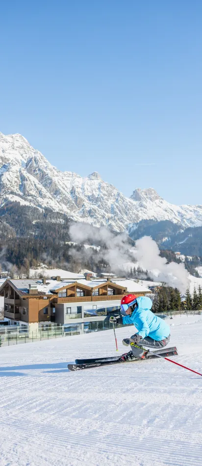 Skifahrer zieht Schwung auf präparierter Piste vor schneebedeckten Alpen und Chalets