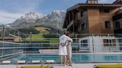 Couple in robes by pool overlooking alpine mountains and wellness hotel