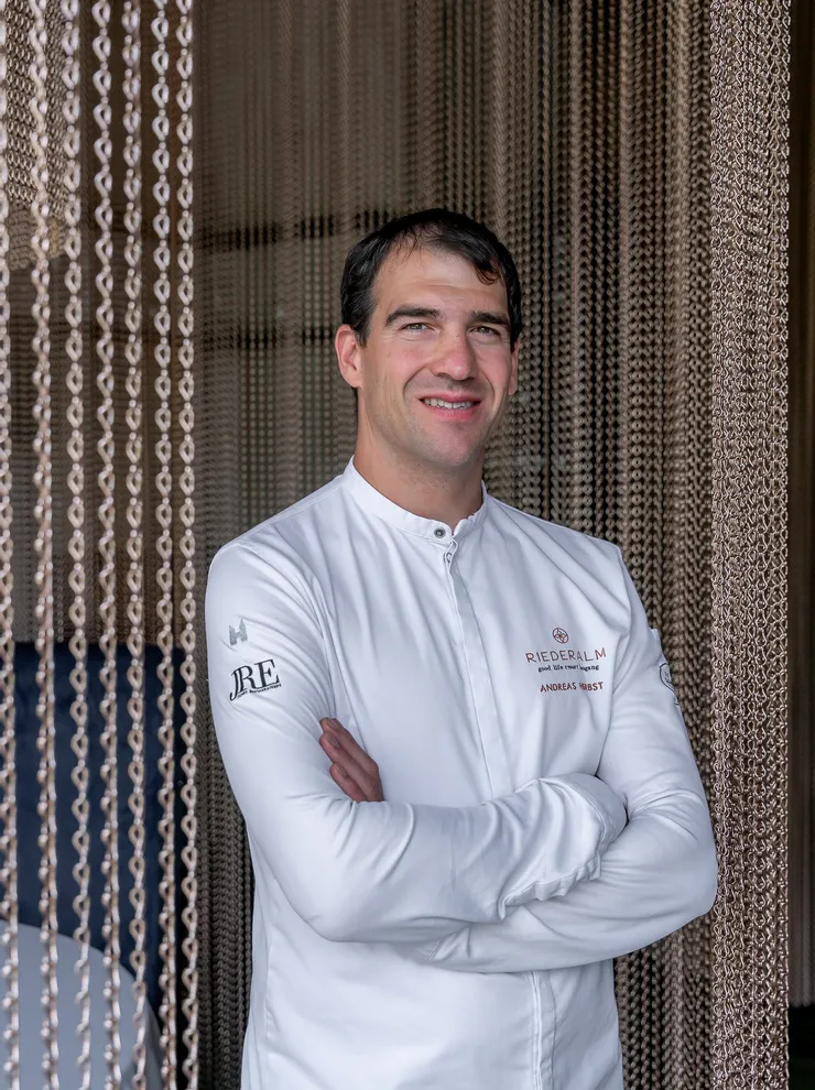 Chef in white Riederalm uniform standing in front of decorative chain curtain