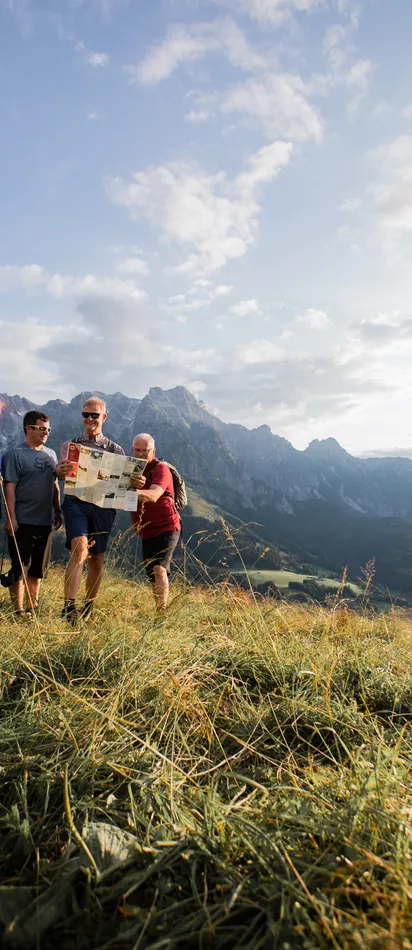 Group of hikers reading a map on a mountain meadow with alpine landscape in background