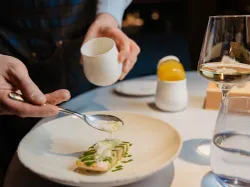 Chef plating gourmet salmon dish with foam and herbs at fine dining restaurant