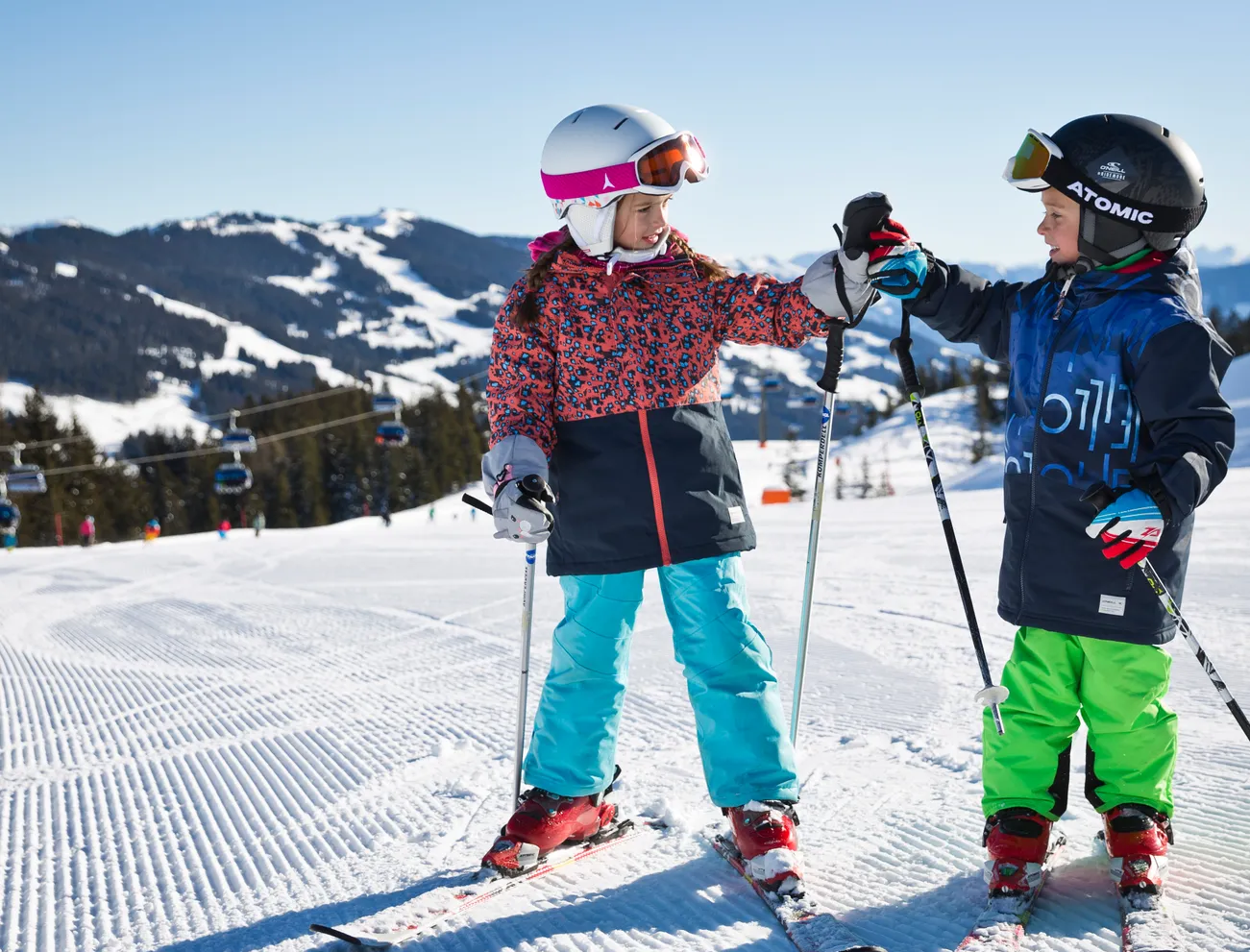Zwei Kinder in bunter Skibekleidung geben sich ein High-Five auf einer verschneiten Skipiste