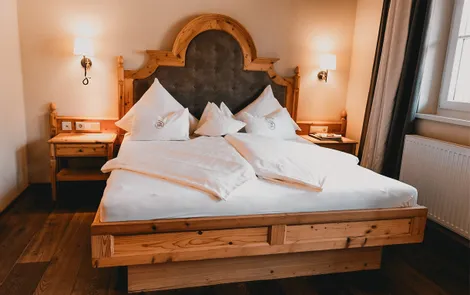 Heimat Gemütliches Hotelzimmer mit großem Holzbett, weißer Bettwäsche und Nachttischen
