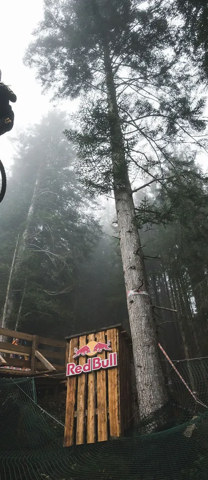 Mountain biker performing high jump off wooden ramp in forest Red Bull event
