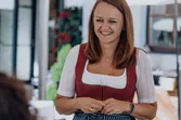 Woman in traditional dirndl dress smiling outdoors on a sunny terrace