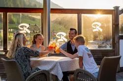 Familie stößt bei Sonnenuntergang auf der Terrasse eines Bergrestaurants mit Getränken an