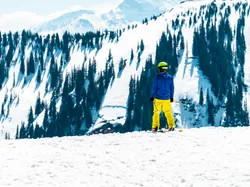 Skifahrer in gelber Hose und blauer Jacke blickt auf verschneite Berglandschaft