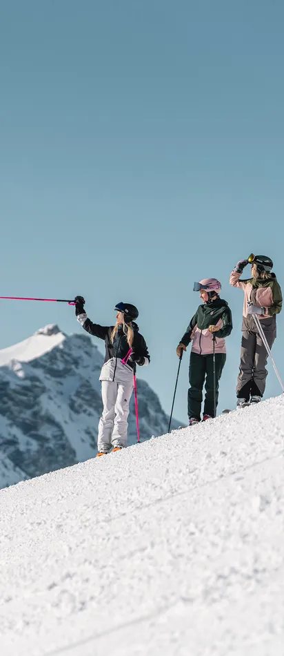 Gruppe Skifahrer auf verschneitem Hang mit Blick auf alpine Gipfel unter klarem blauen Himmel