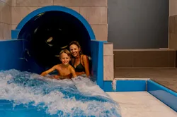 Lächelnde Mutter und Kind rutschen aus einer Indoor-Wasserrutsche im Wasserpark