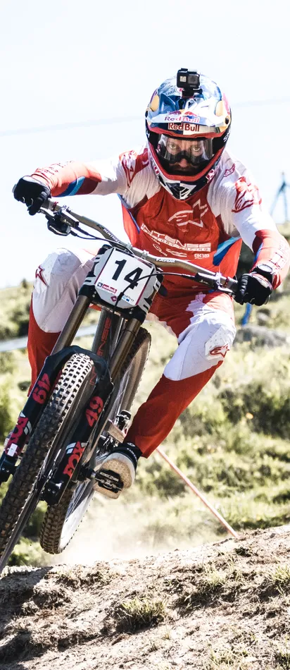 Downhill-Mountainbiker fährt mit roter Ausrüstung und GoPro-Helm über felsigen Trail