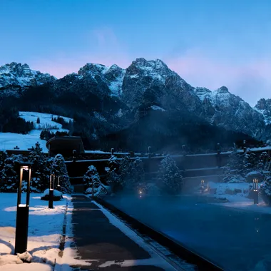 Heated outdoor pool in snowy mountain resort at dusk with scenic alpine backdrop