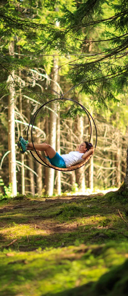 Frau entspannt auf einer hängenden runden Schaukel im sonnenbeschienenen Wald