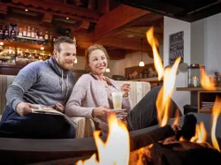 Happy couple relaxing by cozy fireplace with drinks in a rustic alpine bar