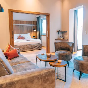 Modern hotel suite with lounge area, velvet armchairs and a cozy bed in natural light