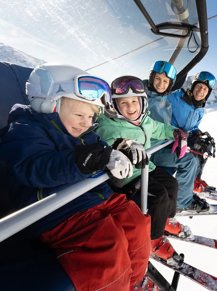 Familie mit Skiausrüstung auf Sessellift im sonnigen Skigebiet
