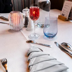 Elegante Restauranttischdekoration mit rotem Cocktail, Wasserkaraffe und baumförmig gefalteter Serviette