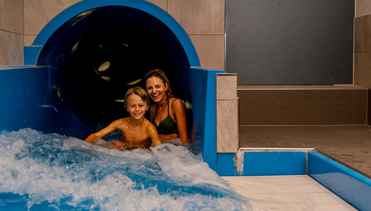 Smiling mother and child exiting indoor water slide at water park