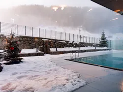 Heated outdoor pool in winter with Christmas trees and snowy mountain backdrop