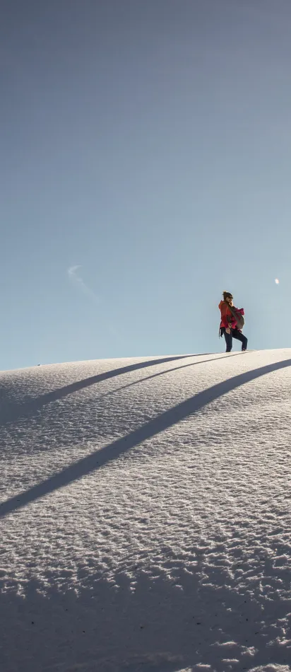 Zwei Menschen wandern bei Sonnenschein durch verschneite Winterlandschaft