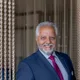 Older businessman with gray beard in blue suit and red tie smiling in front of chain curtain