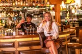 Smiling woman with wine glass sitting at cozy bar while bartender prepares cocktails