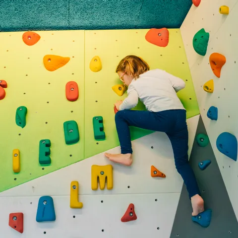 Child climbing indoor bouldering wall with colorful holds shaped like letters