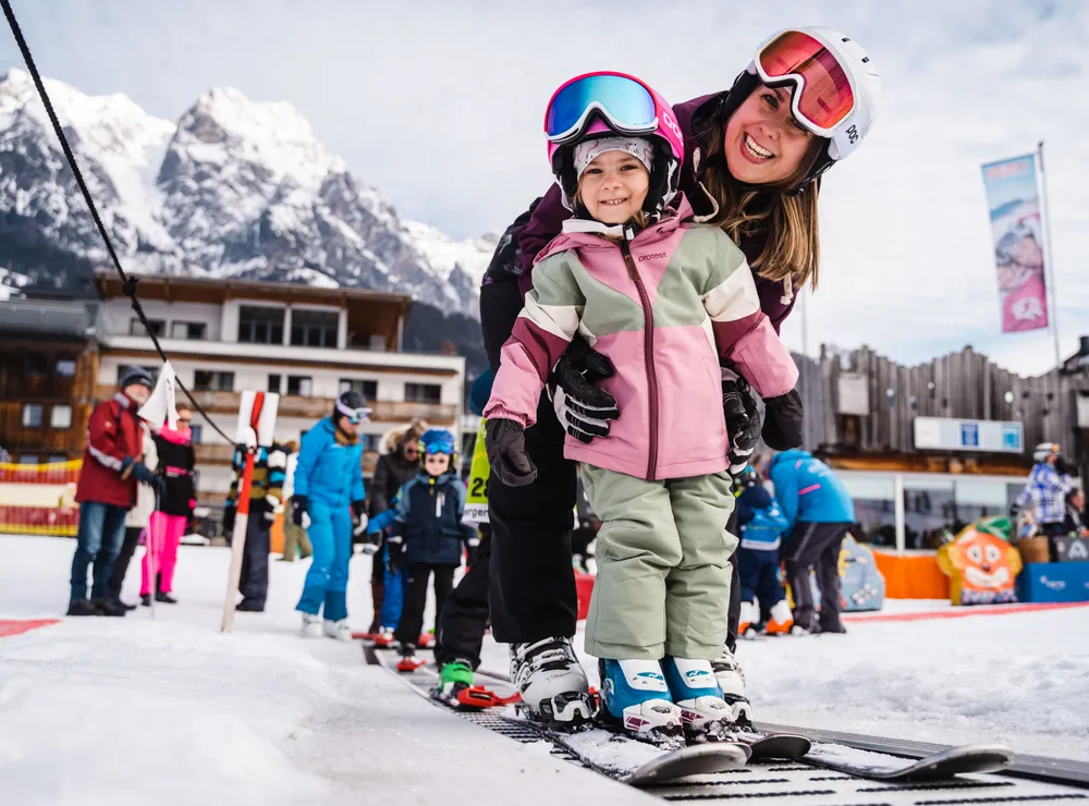 Smiling child learning to ski with instructor on snowy slope at ski resort