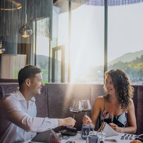 Paar genießt romantisches Abendessen mit Wein in elegantem Restaurant bei Sonnenuntergang