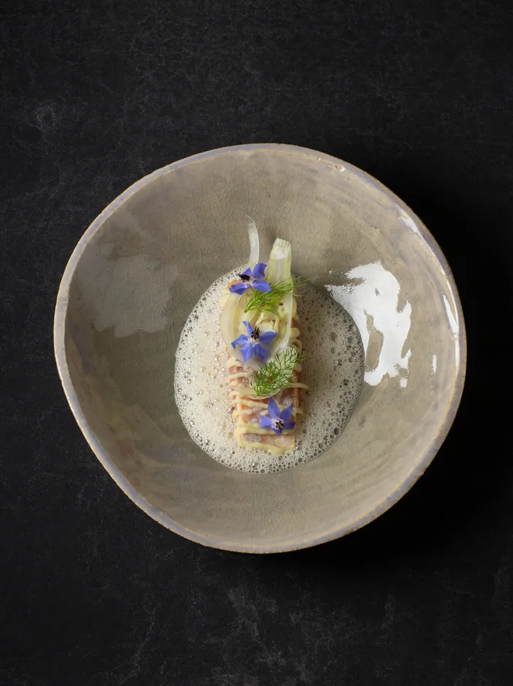 Gourmet-Pastagericht mit Schaum, Fenchel und essbaren blauen Blüten in Keramikschale