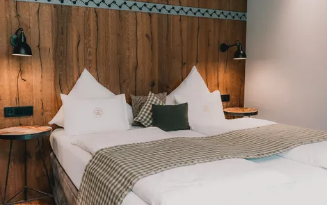 Gemütliches Hotelzimmer mit Doppelbett, Holzwand und moderner Beleuchtung