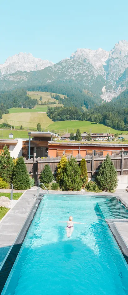 Outdoor swimming pool with sun loungers at hotel resort overlooking alpine mountains