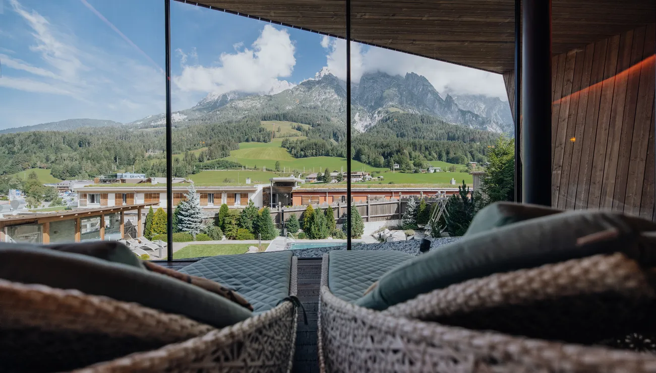 Panoramablick auf Alpenhotel, grüne Hügel und Berge durch Glasfront vom Spa-Ruheraum