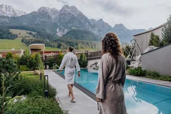 Paar in Bademänteln am Außenpool eines Alpen-Wellnesshotels mit Bergblick