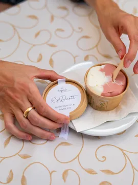 Frau isst Buttermilch-Himbeer-Eis aus einem umweltfreundlichen Becher auf dekorierter Tischdecke