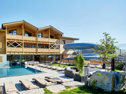 Alpenresort mit Außenpool, Holzfassade und großer Wasserrutsche im Sonnenschein