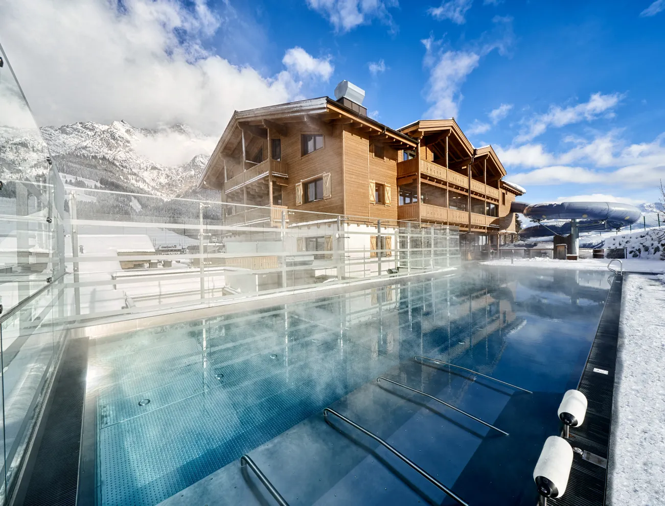 Beheizter Außenpool im Skigebiet mit Holzchalet und verschneiter Bergkulisse