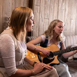 Two women in traditional dresses singing together, one playing an acoustic guitar