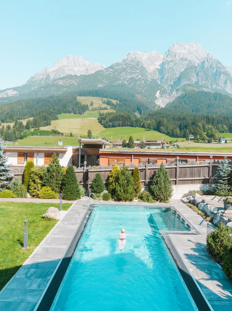 Outdoor swimming pool with sun loungers at hotel resort overlooking alpine mountains