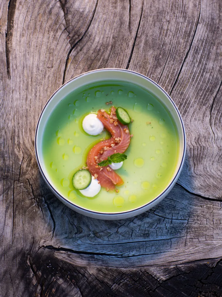 Grüne Gurkensuppe mit rohem Lachs, Creme und Kräutern in einer Schüssel auf rustikalem Holz