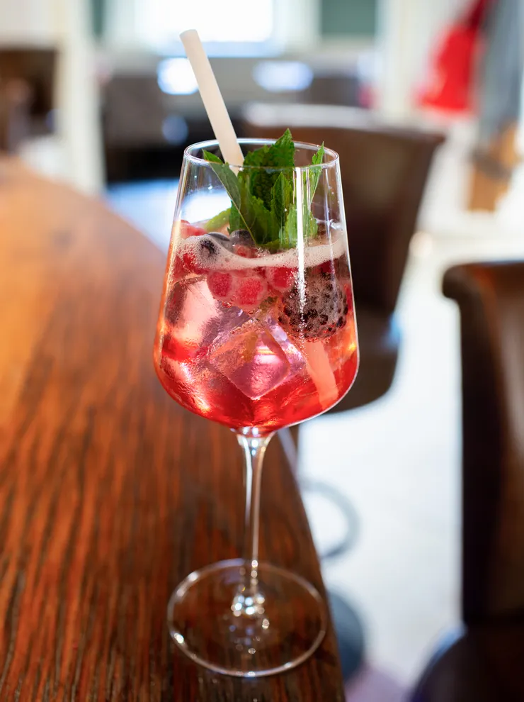Erfrischender Beeren-Cocktail mit Eis und Minze im Weinglas auf Holztheke