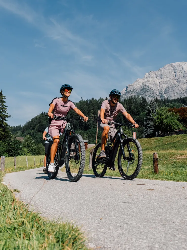 Paar fährt E-Mountainbikes auf einem alpinen Panoramaweg im Sommer