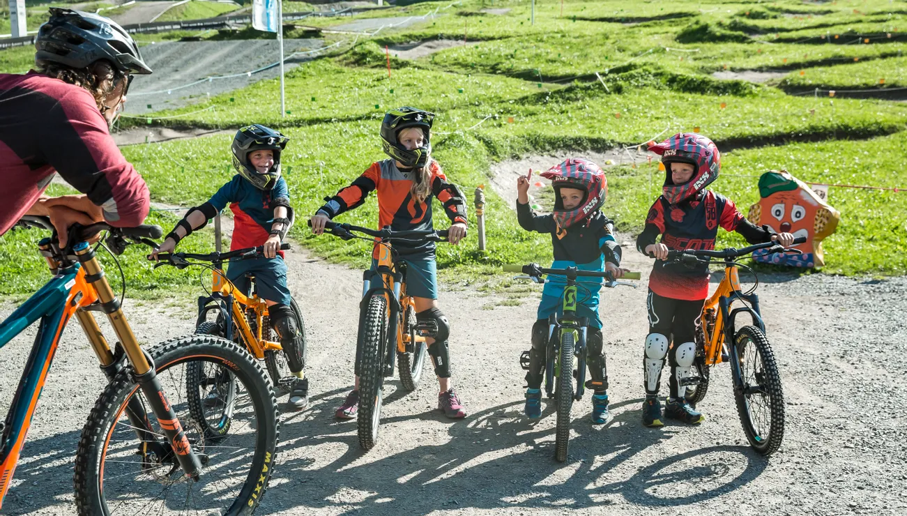 Kids in protective gear on mountain bikes talking with adult at bike park