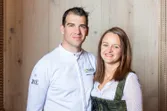 Chef in white uniform standing next to smiling woman in traditional dress
