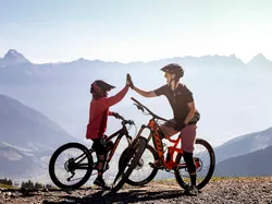 Zwei Mountainbiker geben sich ein High Five auf einem Trail mit Bergblick