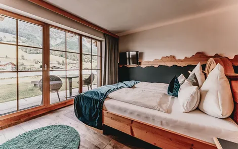 Modernes Hotelzimmer mit Holzbett, Alpenblick durch große Fenster und Balkonmöbeln